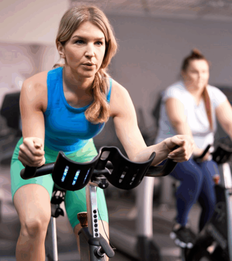 Women participating in a high-energy indoor cycling class at Women's Fitness Clubs of Canada, focused on cardio endurance and full-body fitness.
