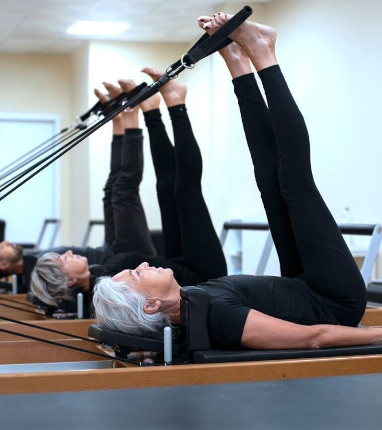 Group of adults participating in a Pilates reformer class at Women's Fitness Clubs of Canada, focusing on core strength and flexibility.